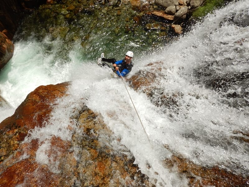 Personne en casque blanc descend en rappel une cascade puissante avec un courant d'eau intense dans un canyon.