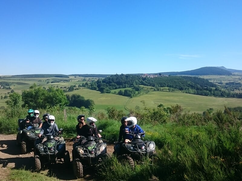 Cinq personnes en quad posant sur un sentier avec une vue panoramique sur la campagne verte et les collines.