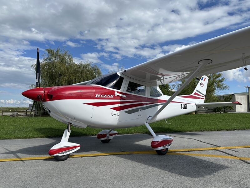 Petit avion léger blanc et rouge stationné sur une piste d'aérodrome sous un ciel partiellement nuageux