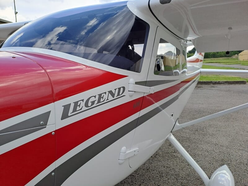 Vue rapprochée de l'aile et de la cabine d'un avion léger blanc et rouge marqué LEGEND sur l'aérodrome de Gray Saint-Adrien.