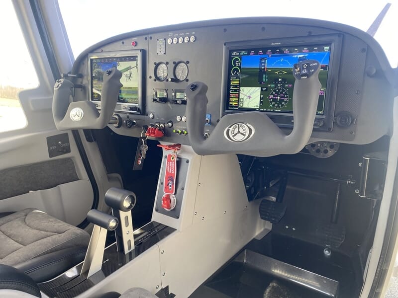 Intérieur d'un avion ultraléger avec deux commandes de vol, sièges en tissu gris et tableau de bord numérique moderne.