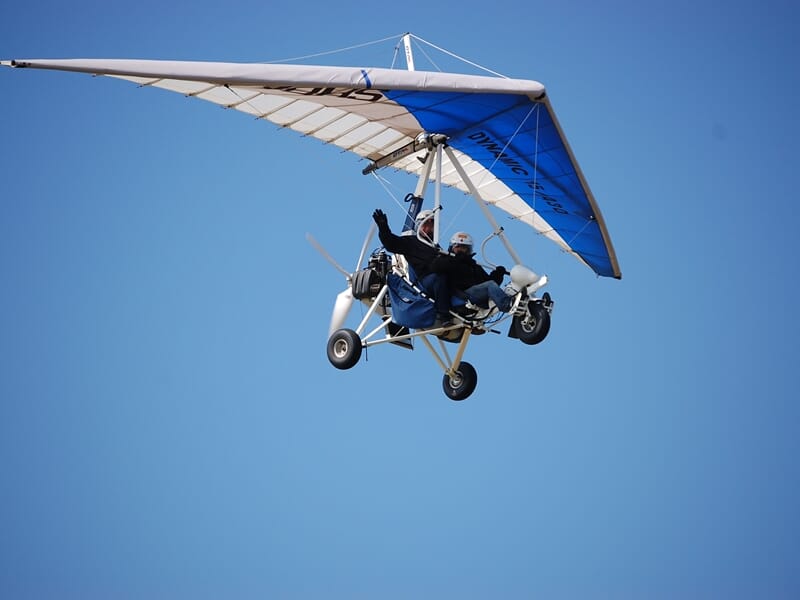 ULM pendulaire biplace avec une aile blanche et bleue en vol lors d'un baptême de l'air en ULM près de Dijon.