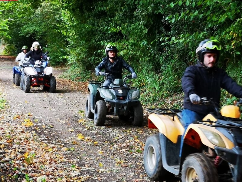 Quads conduits par plusieurs personnes sur un sentier forestier couvert de feuilles mortes en automne.