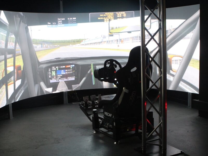 Simulateur de conduite automobile avec siège, volant et grand écran incurvé affichant une piste de course.