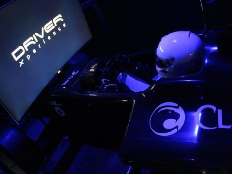 Simulateur de course avec casque blanc posé, éclairage bleu et écran affichant Driver Xperience.