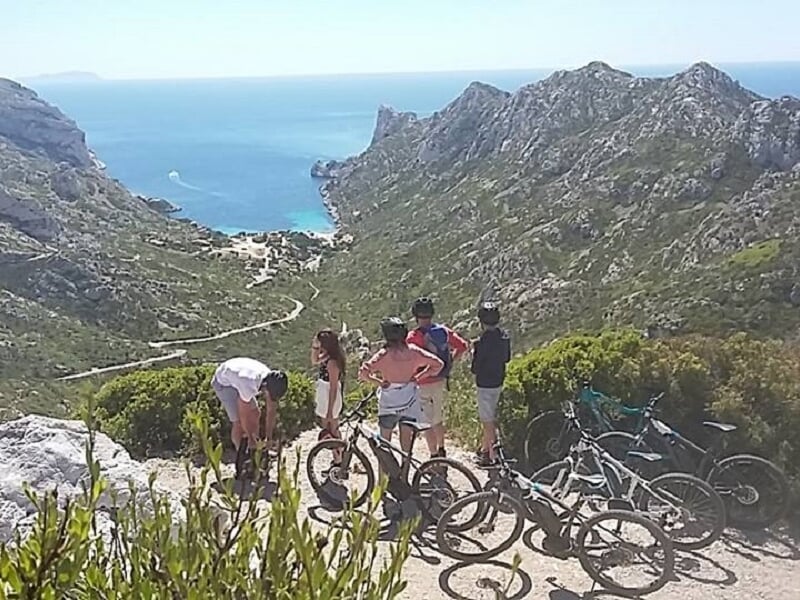 Groupe de cyclistes en VTT en pause sur un sentier en hauteur avec vue panoramique sur la mer et les falaises.