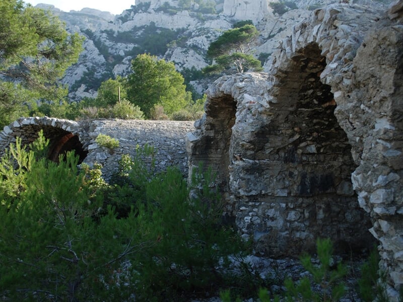 Ancien mur en pierre avec arches dans un paysage naturel boisé, typique des calanques près de Marseille.