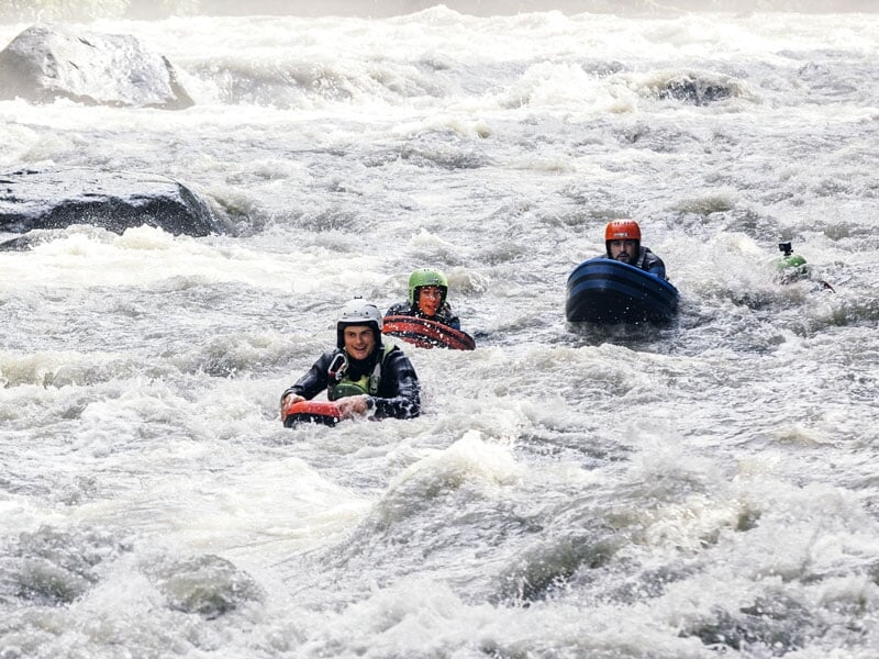 Groupe de trois personnes en hydrospeed naviguant une rivière tumultueuse, portant des casques et des gilets de sauvetage, flottant à travers les rapides avec des flotteurs de couleurs différentes