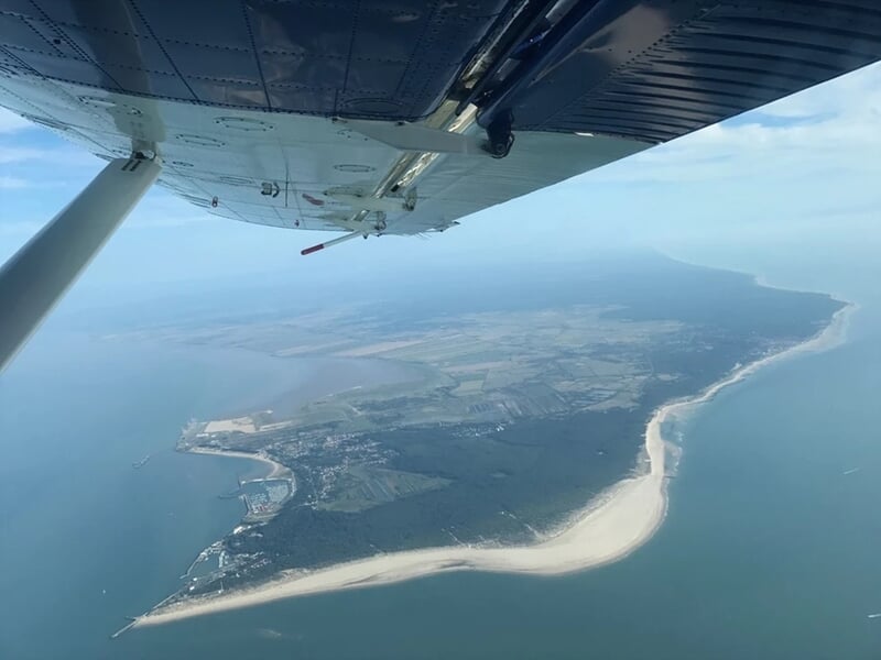 Vue aérienne depuis un avion au-dessus d'une côte avec une plage et une mer calme sous un ciel clair.