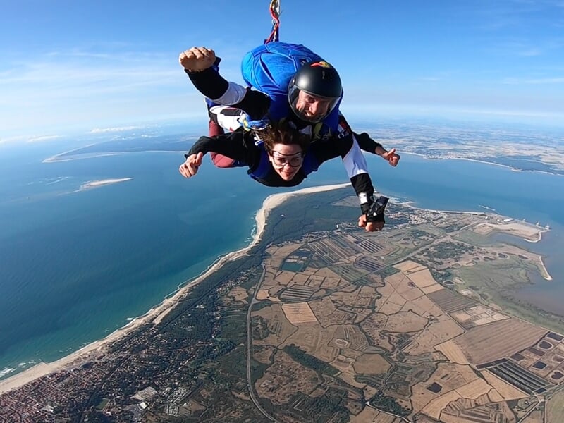 Parachutisme en tandem au-dessus d'une côte avec des terres agricoles, une plage et la mer sous un ciel dégagé.