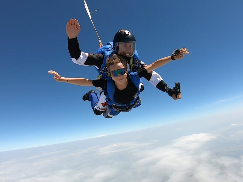 Deux personnes en parachutisme en tandem en chute libre au-dessus des nuages avec un ciel bleu clair.