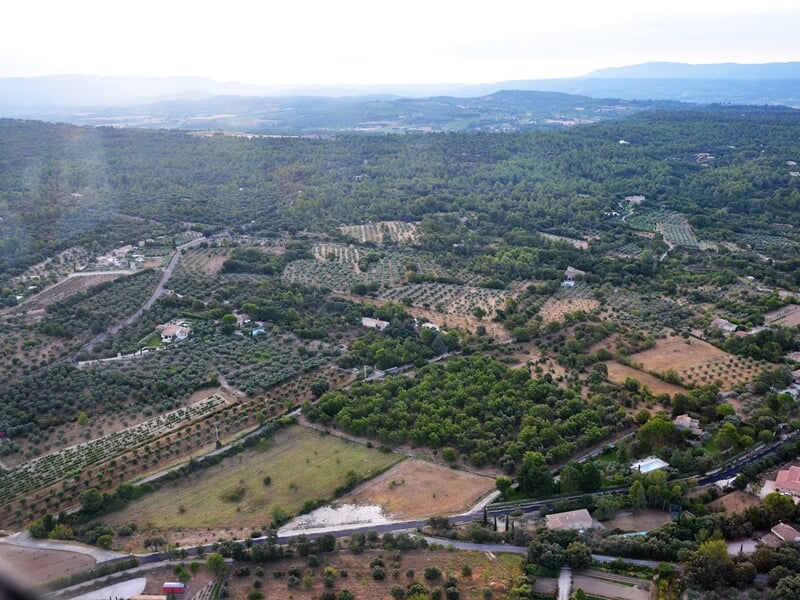 Paysage vu du ciel montrant une campagne verdoyante avec des champs, des arbres et quelques maisons dispersées.