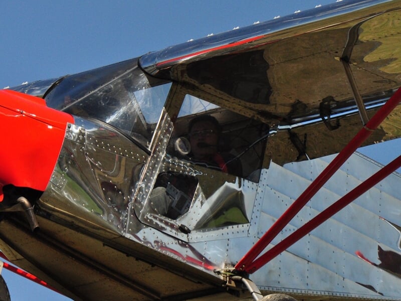 Gros plan sur un pilote dans un petit avion ultraléger avec une structure métallique et une cabine vitrée.