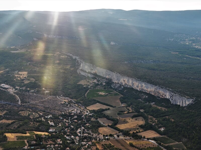 Vue aérienne d'un paysage rural avec des champs, des collines et un effet de lumière solaire traversant le ciel.
