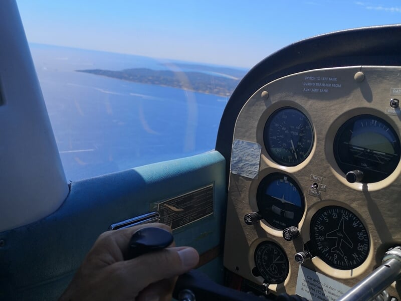Vue depuis le cockpit d'un petit avion survolant la mer et une île au loin sous un ciel clair.