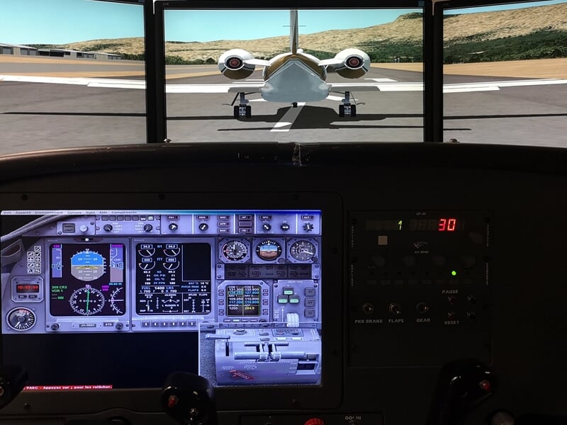 Cockpit d'un simulateur de vol avec écrans et commandes, vue sur un avion sur la piste.