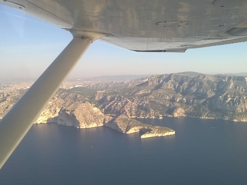 Vue aérienne d'une côte rocheuse avec des montagnes et la mer, prise depuis un petit avion.