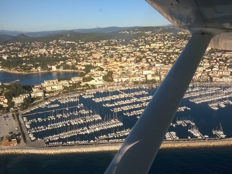 Vue d'un port de plaisance avec de nombreux bateaux et une ville en arrière-plan, prise depuis un avion.
