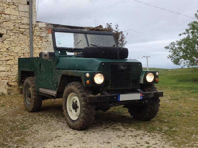 Ancien véhicule tout-terrain vert foncé garé sur un chemin de terre dans un paysage rural.