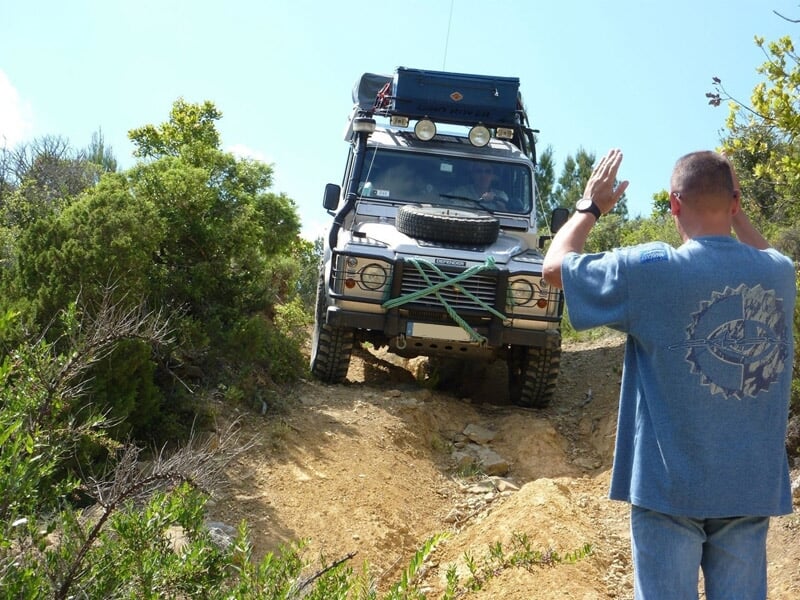 Véhicule tout-terrain blanc avec équipement sur le toit, homme en t-shirt bleu guidant la manœuvre.
