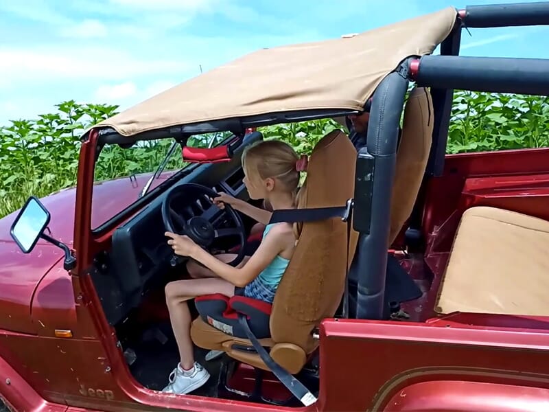 Une jeune fille en robe et en basket conduit un jeep sur un terrain de 4x4 