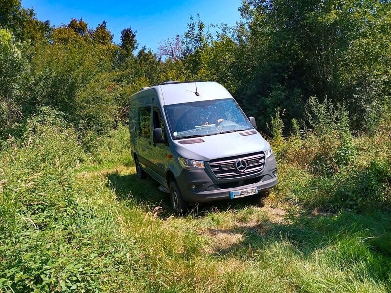 Fourgon Mercedes gris circulant sur un sentier herbeux au milieu d'une végétation dense et verdoyante