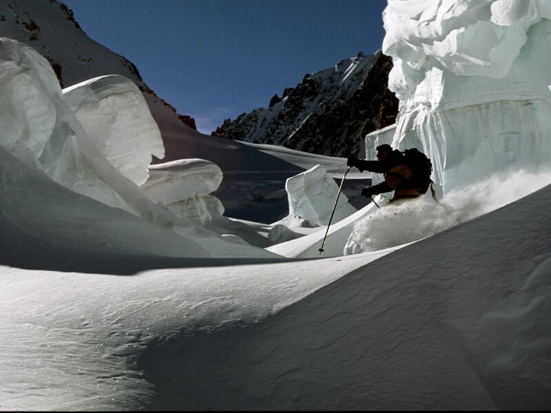 Skieur évoluant entre de grandes formations de neige sculptée, dans un paysage montagneux ensoleillé.