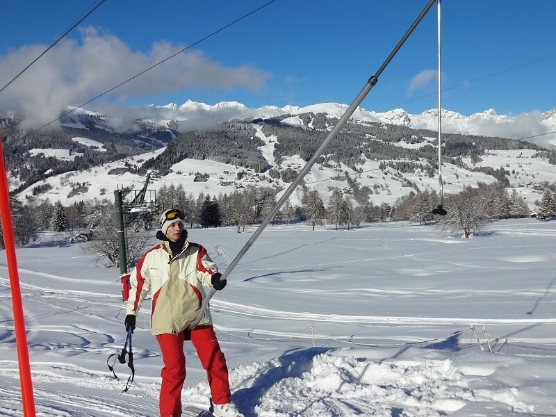 Personne en tenue de ski tirant sur une remontée mécanique dans un paysage enneigé et ensoleillé.