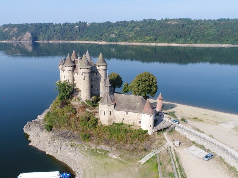 Château médiéval sur une presqu'île entourée d'un lac calme et de collines boisées.