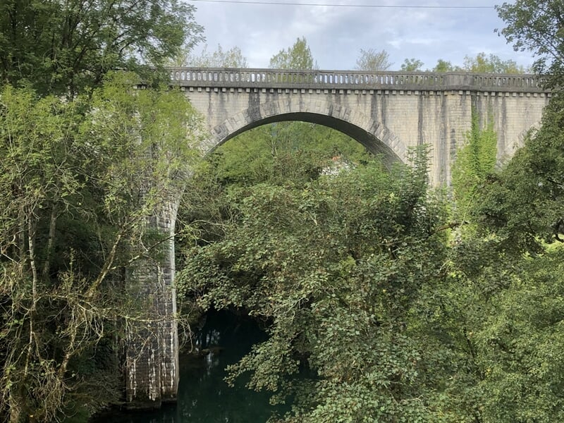 Un pont en pierre ancien entouré d'arbres verts au-dessus d'une rivière calme dans un paysage naturel.