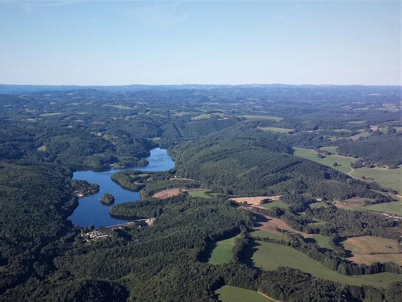 Vue aérienne d'un paysage verdoyant avec un lac sinueux entouré de forêts et de champs sous un ciel clair.