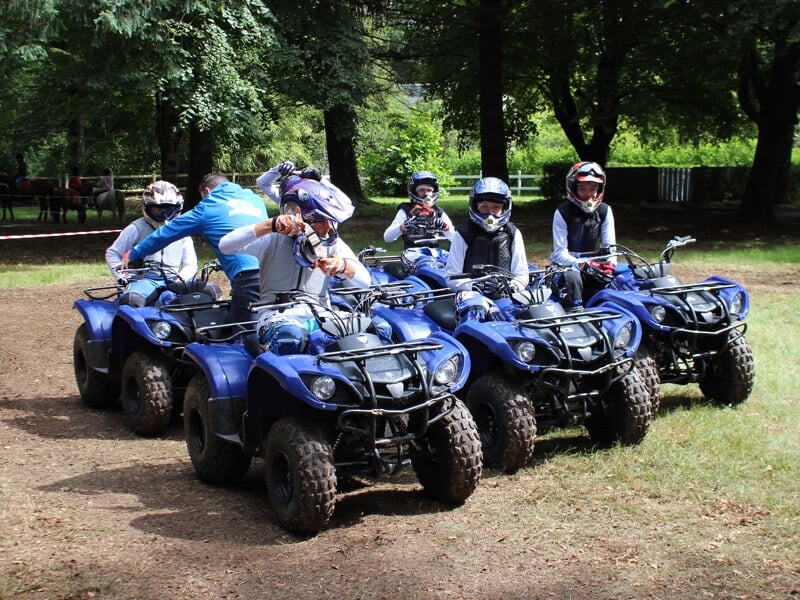 Groupe de jeunes en tenue de protection prêts pour une randonnée en quad dans un cadre boisé et ensoleillé.