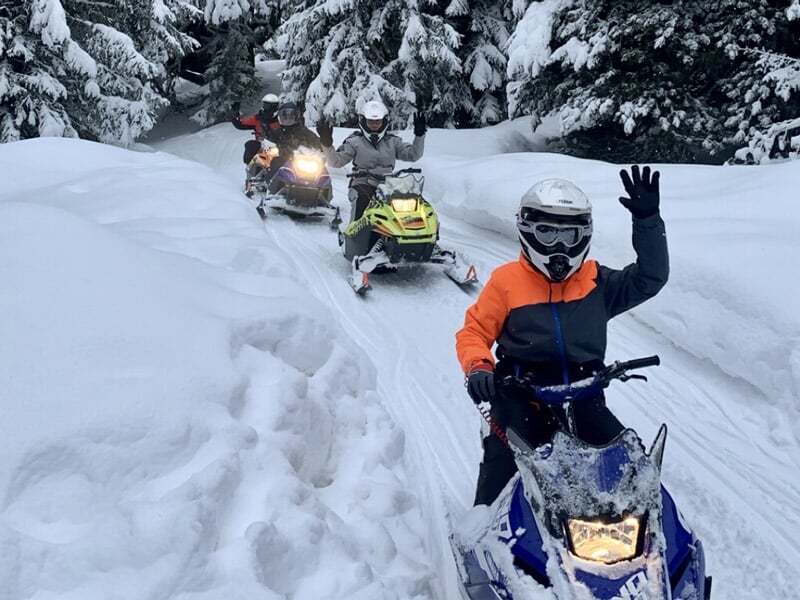 Groupe de motoneiges avec des conducteurs en tenue d'hiver roulant sur un chemin enneigé.