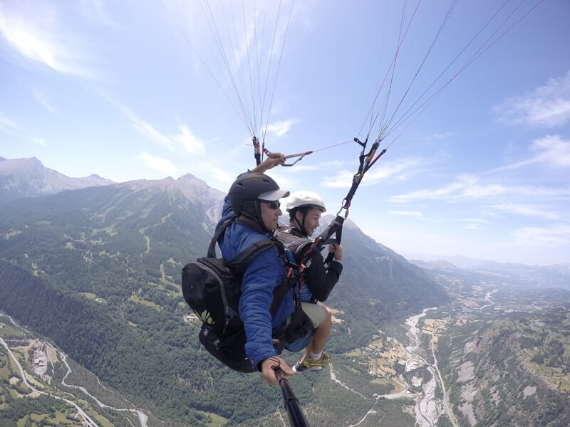 Parapente en vol au-dessus d'une vallée verdoyante, montagnes en arrière-plan, sous un ciel bleu