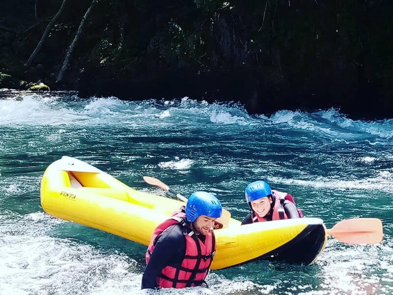 Deux personnes en gilets de sauvetage et casques bleus dans une eau vive avec un raft jaune renversé.