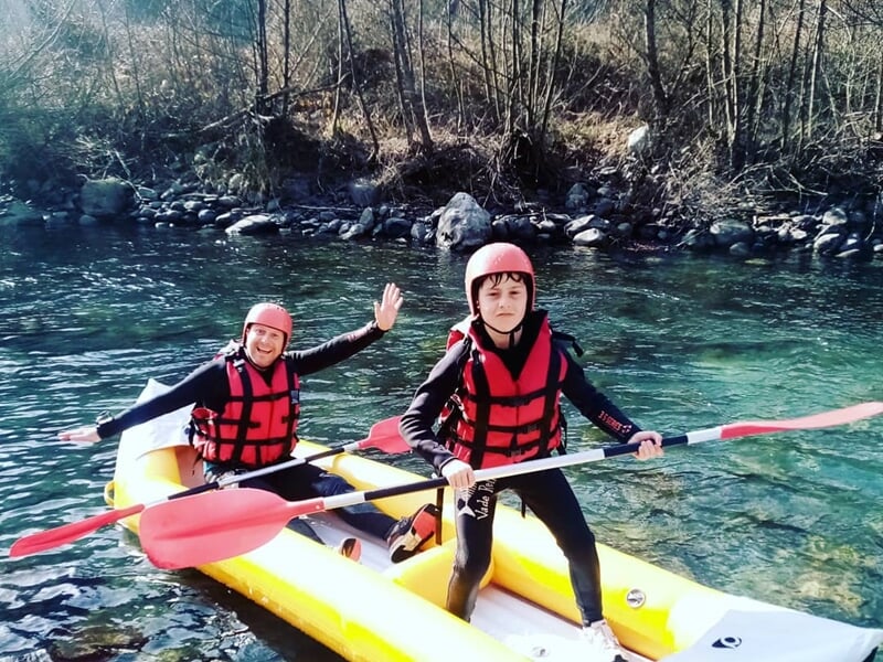 Deux jeunes en gilets de sauvetage rouges sur un raft jaune dans une rivière claire entourée d'arbres.