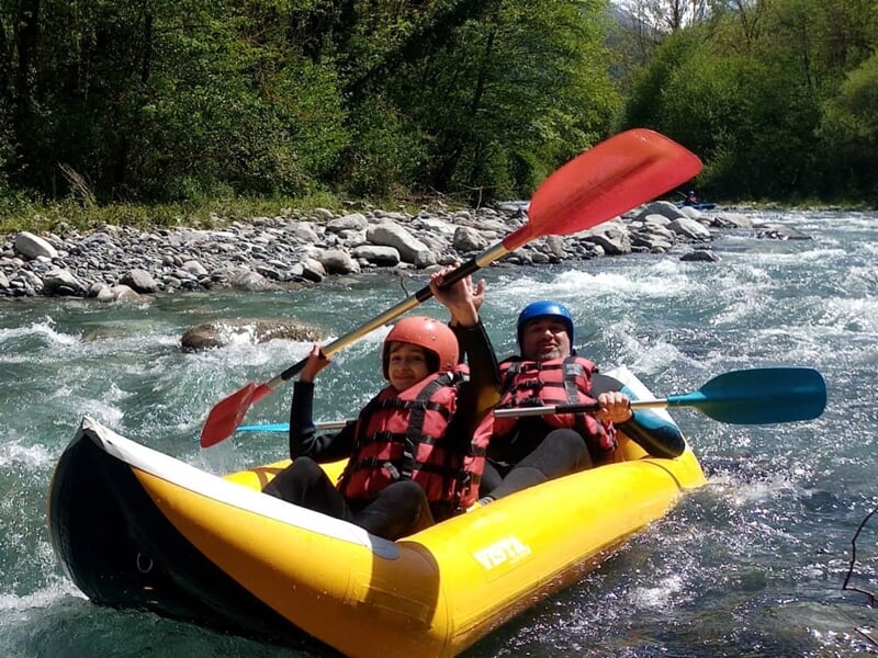 Deux personnes en raft jaune pagayant avec des pagaies rouges et bleues sur une rivière à courant modéré.