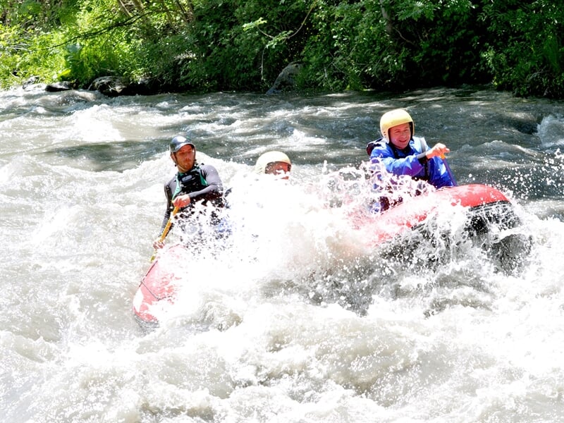 Groupe de personnes en raft jaune pagayant dans une rivière avec des rapides et éclaboussures d'eau.