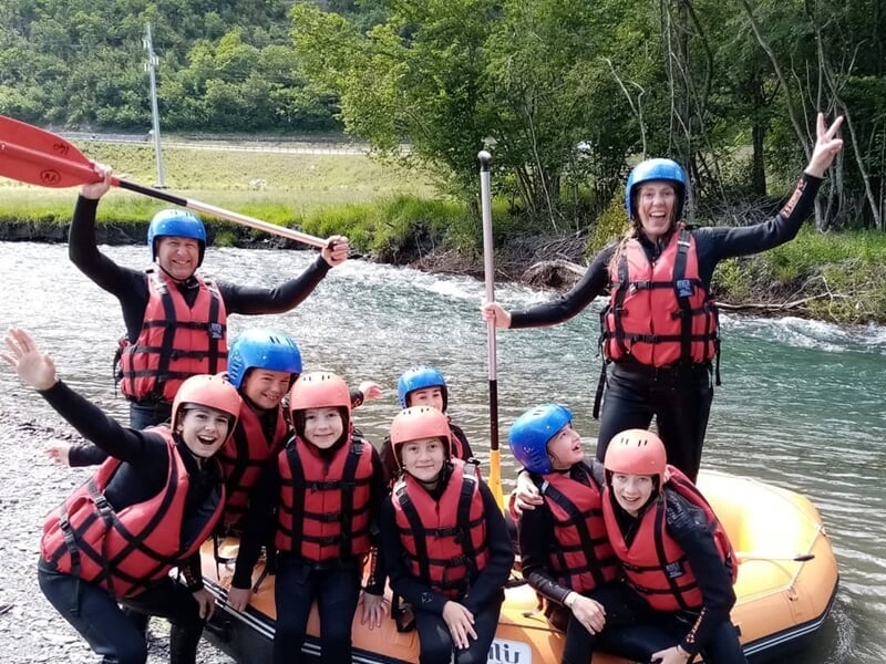 Groupe de personnes en raft jaune pagayant avec énergie dans une rivière à courant rapide et éclaboussures.