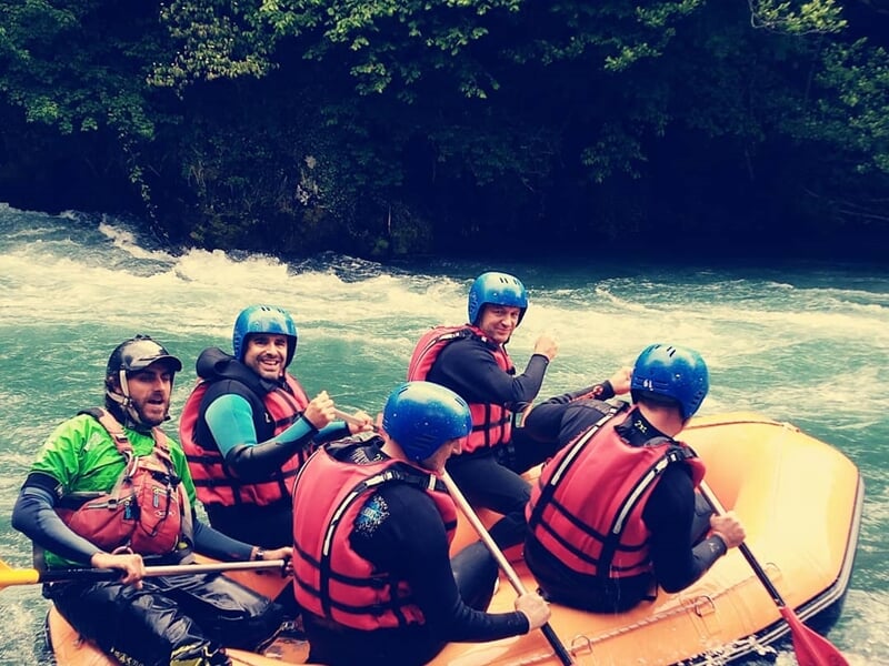 Cinq personnes en raft jaune souriantes et levant les bras en signe de victoire sur une rivière calme.