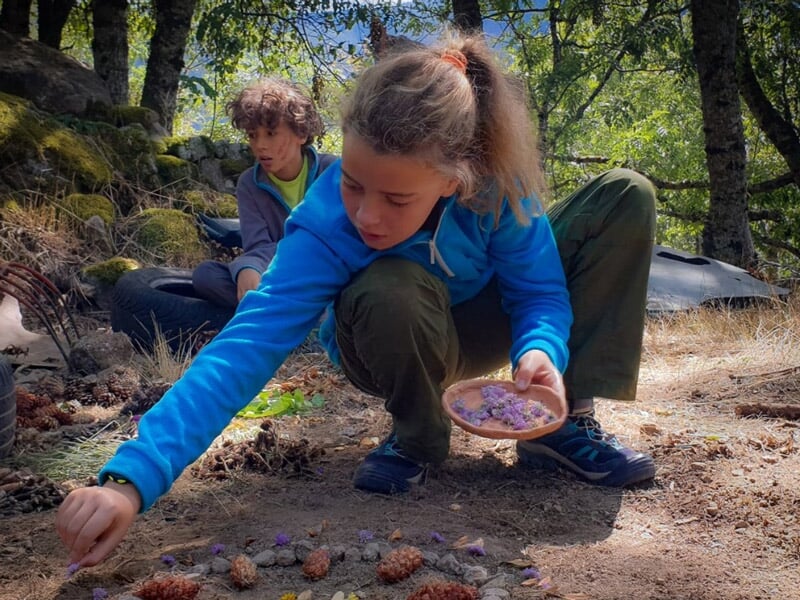 Jeune fille en tenue bleue arrange des éléments naturels sur le sol en forêt lors d'un stage de survie.