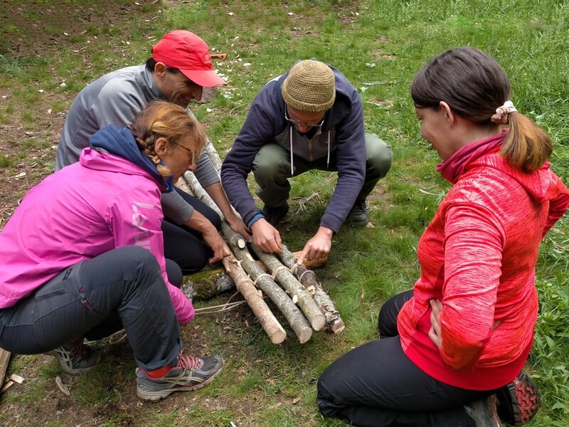 Quatre personnes en plein air assemblent des branches de bois pour un feu ou un abri en stage de survie.