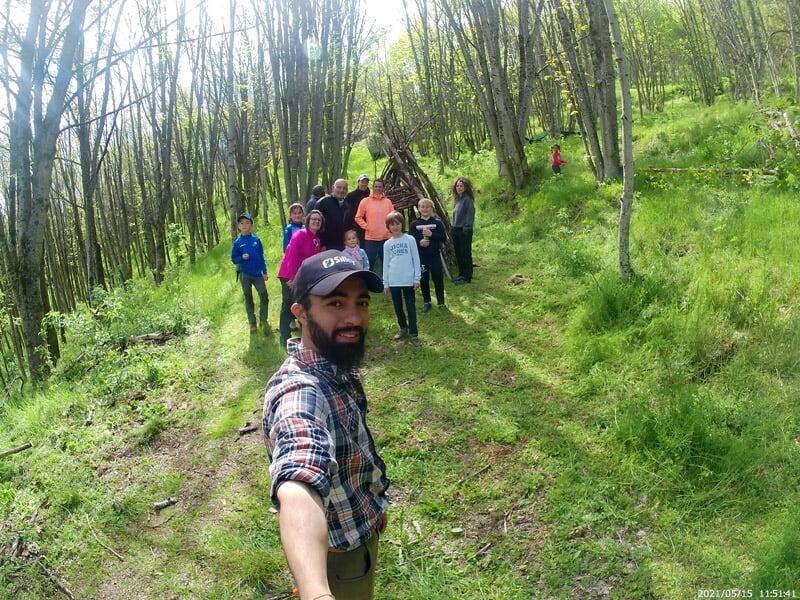 Groupe de personnes en randonnée dans une forêt verdoyante, guidé par un homme barbu en chemise à carreaux.