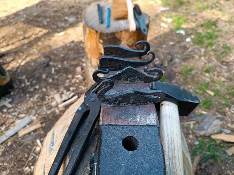 Outils en métal forgé posés sur une enclume avec un marteau et un fond de forêt en arrière-plan.