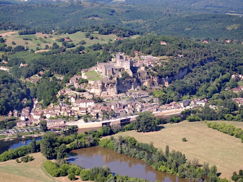 Vue aérienne d'un village médiéval avec un château fort perché sur une colline entourée de verdure.