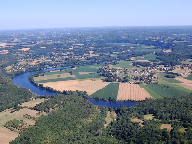 Paysage vu du ciel montrant une rivière sinueuse traversant des champs cultivés et des forêts verdoyantes.