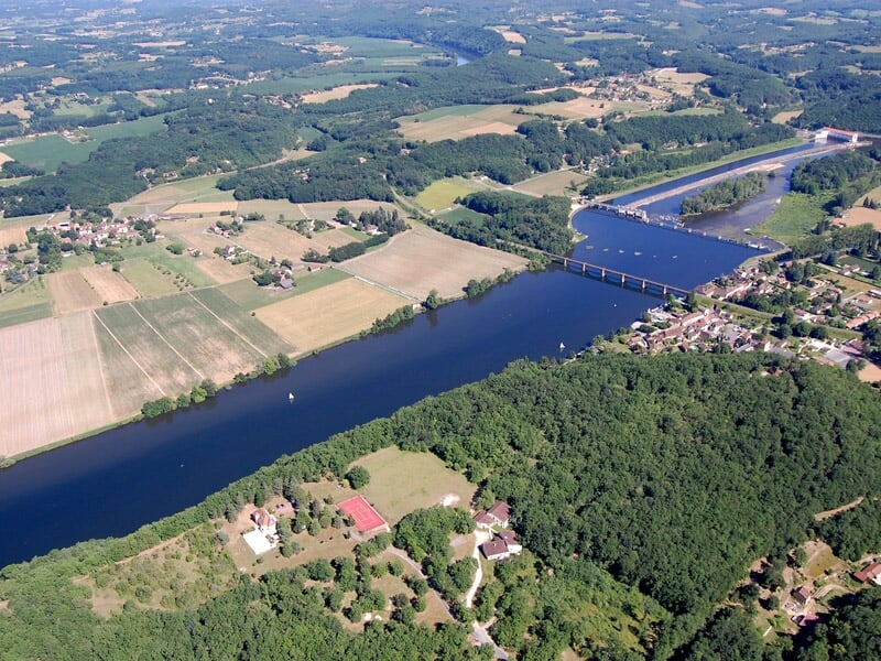 Vue aérienne d'un pont enjambant une large rivière avec des maisons et des champs autour.