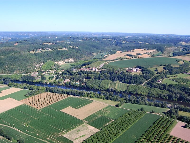 Paysage rural vu du ciel avec des champs cultivés, des vergers et une rivière serpentant au loin.