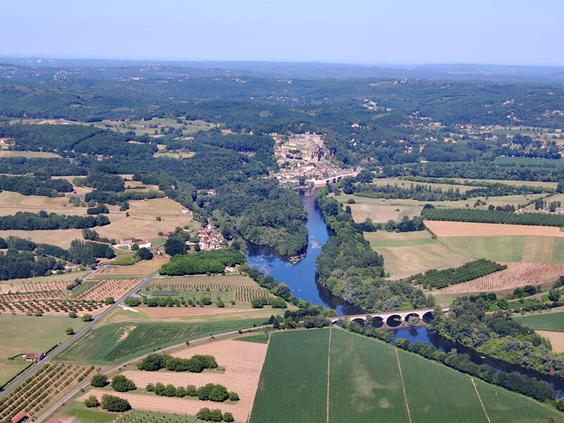 Vue aérienne d'une rivière traversant une campagne vallonnée avec un pont en pierre et des villages.