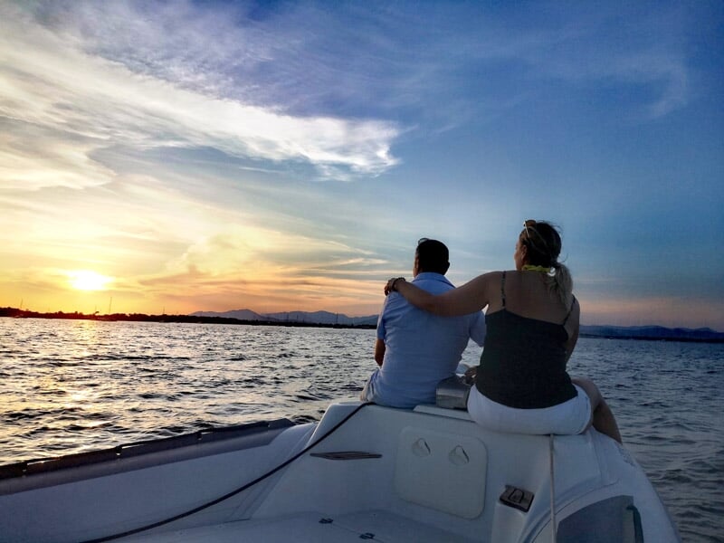 Couple assis à l'avant d'un bateau regardant un coucher de soleil sur la mer avec un ciel partiellement nuageux.